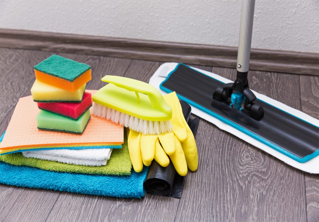 Pile of rags, sponges, a scrub brush, some gloves, and a roll of trash bags on the ground next to a mop