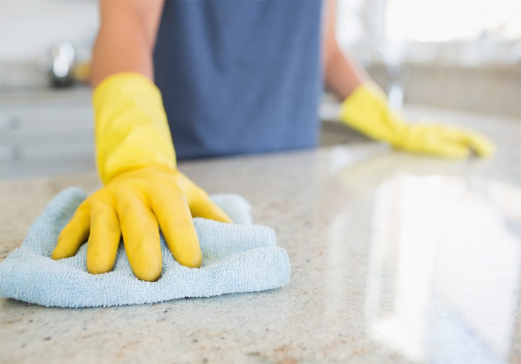 Close up on yellow gloved hands, cleaning granite countertop